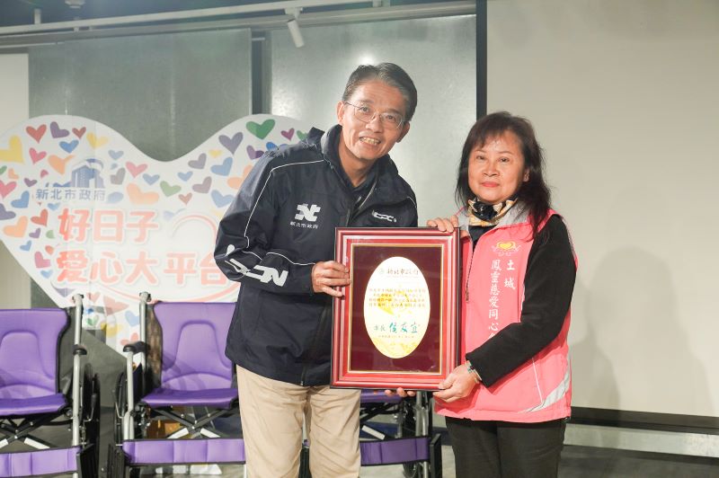 善心企業團體讓愛輪轉 9單位合捐新北305台輪椅 6 《圖說》新北市府秘書長邱敬斌(左)代表侯友宜市長回贈感謝牌給土城鳳靈慈愛同心會理事長黃妙鳳。〈社會局提供〉