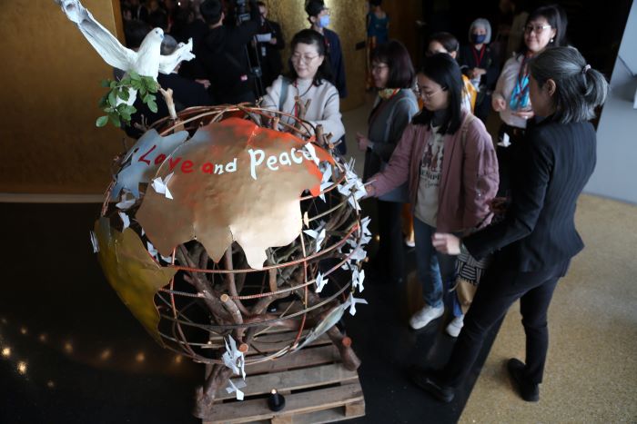 《圖說》參與「和諧同行、青年朝聖之旅」的代表一一在漂流木地球裝置上掛上和平鴿。〈宗博館提供〉