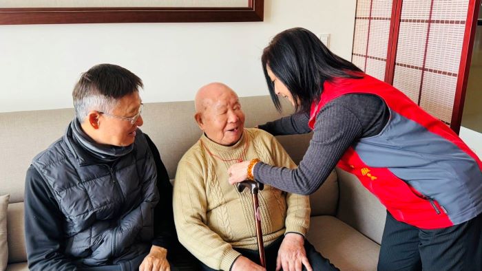 新北榮服處暖訪中和百歲榮民 長輩開心讚「Very Good」 5 《圖說》王玟琳組長(右)代表致贈金壽桃,親自為郭爺爺(中)戴上,向郭爺爺祝賀壽誕。〈新北榮服處提供〉